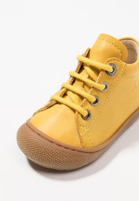 Scarpa in pelle gialla con punta tonda, suola in gomma e design con lacci. Presenta occhielli metallici e una suola testurizzata per una migliore presa.