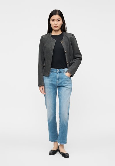 Svart denimjacka med rund hals och tryckknappstängning, kombinerad med ljusblå jeans med rakt ben och svarta ballerinaskor.