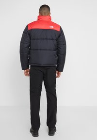 Giacca puffer da uomo con corpo nero e pannello superiore rosso, caratterizzata da una texture trapuntata, colletto alto e logo The North Face sulla schiena.