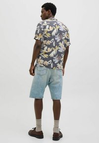 Chemise à manches courtes avec un motif floral dans des tons de gris, jaune et violet ; assortie à un short en denim bleu clair et des chaussures marron.