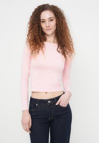 Φωτεινό ροζ, μακρυμάνικο κοντό τοπ με τετράγωνη λαιμόκοψη, σε συνδυασμό με σκούρο τζιν. Λείο ύφασμα και στενή γραμμή.