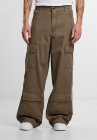 Brune cargo bukser lavet af bomuld, med flere lommer, en løs pasform og en knaplukning. Båret med hvide sneakers.