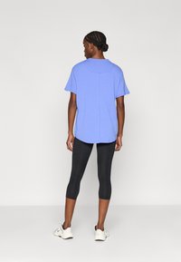 Μπλε ανοιχτό κοντομάνικο μπλουζάκι με στρογγυλή λαιμόκοψη, φορεμένο πάνω από μαύρα κολάν, σε συνδυασμό με λευκά αθλητικά παπούτσια. Η πίσω όψη δείχνει άνετη εφαρμογή.