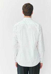 Weißes Langarmhemd mit Button-Down-Kragen, mit abgerundetem Saum und Zwei-Button-Manschetten. Glattes Material, ohne sichtbare Muster.