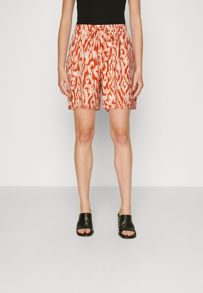 Femme portant un short à cordon de serrage à motifs orange et blanc, assorti à un débardeur noir et des sandales noires à bout ouvert.