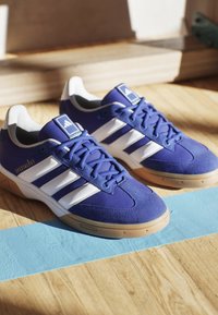 Blå atletiske sko lavet af mesh og suede, med tre hvide striber, en gummisål og "Spezialist" tekst på siden.