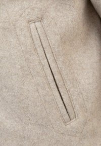 Beež villane müts, millel on tekstureeritud pind, horisontaalne tasku, millel on ristkülikukujuline ava ja peened õmbluse aktsendid.