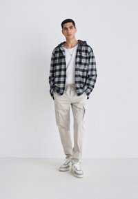 Black and white plaid flannel jacket over a white shirt, paired with beige cargo pants and gray sneakers. Minimalist design, casual fit.