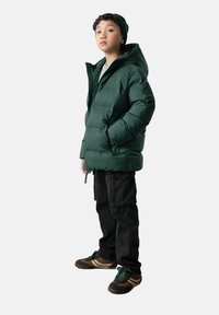 Zielona kurtka puchowa z kapturem, z zamkiem błyskawicznym i kieszeniami po bokach, zestawiona z czarnymi spodniami cargo i ciemnymi sneakerami z zielonymi akcentami.