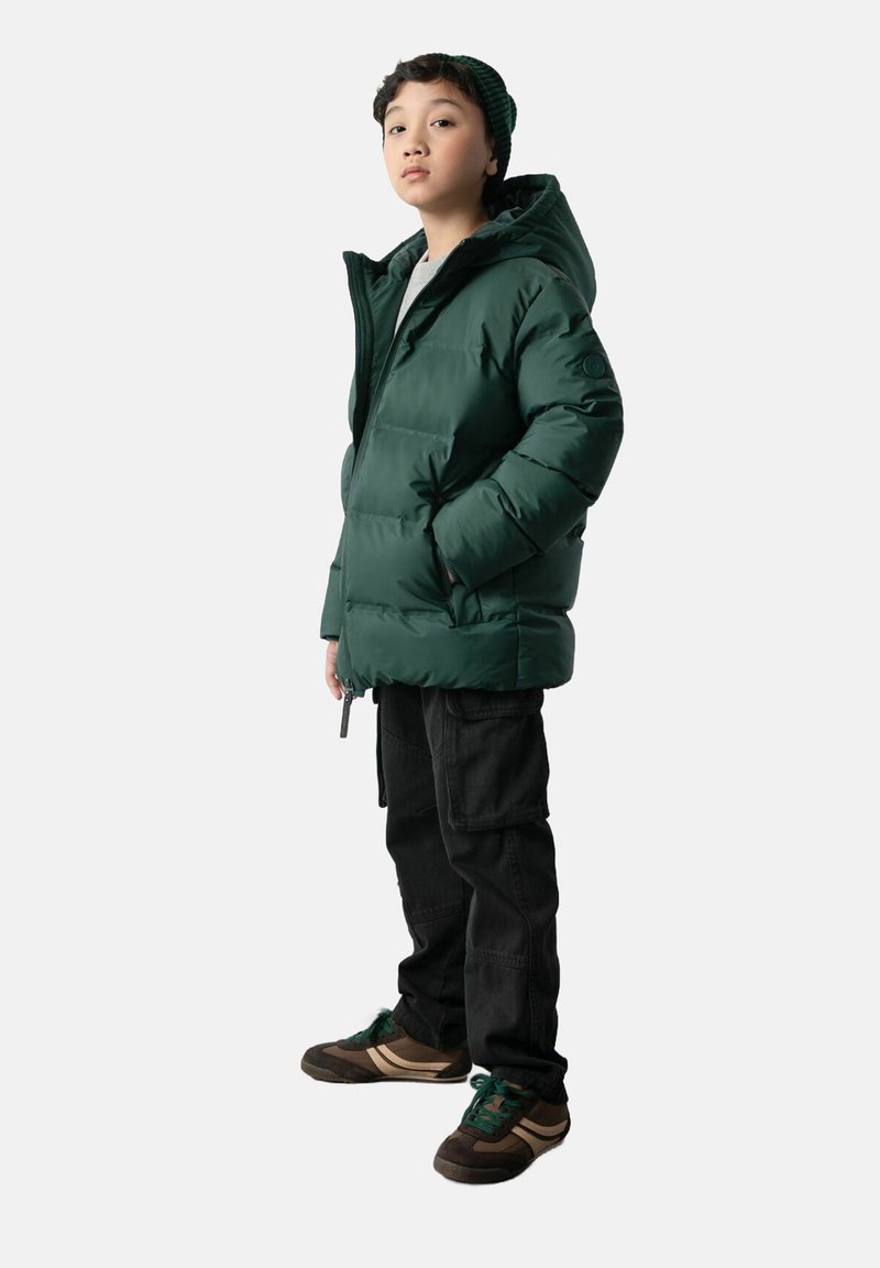 Zielona kurtka puchowa z kapturem, z zamkiem błyskawicznym i kieszeniami po bokach, zestawiona z czarnymi spodniami cargo i ciemnymi sneakerami z zielonymi akcentami.