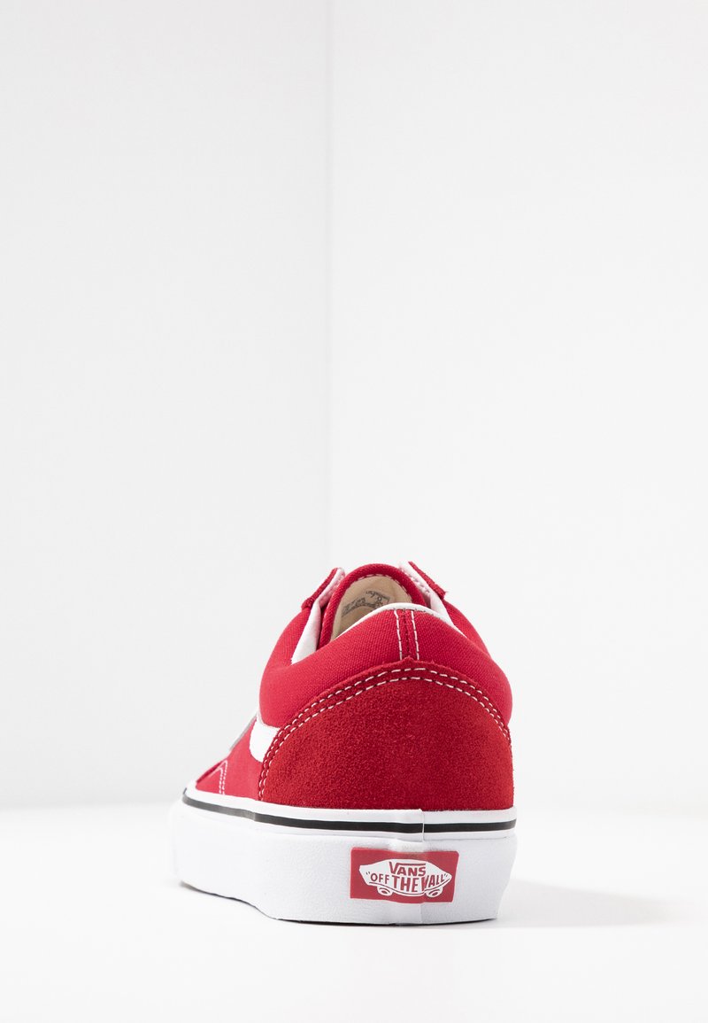 Zapatilla de ante rojo con una franja lateral blanca y suela negra. Presenta un cuello acolchado y el logo de Vans en el talón. Materiales texturizados visibles.