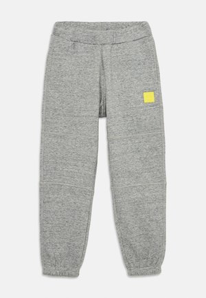 Grå joggebukser laget av myk stoff, med en elastisk midje og en liten gul logo-patch på venstre hofte. Tapered ben-design.