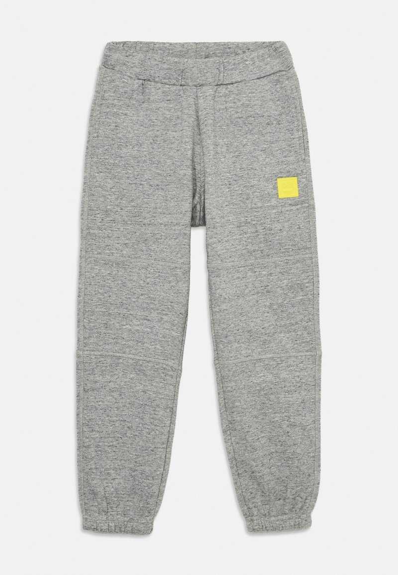 Graue Sweatpants aus weichem Material, mit elastischem Bund und einem kleinen gelben Logo-Patch an der linken Hüfte. Mit schmal zulaufendem Bein.