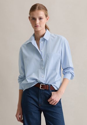 Lichtblauw overhemd met knopen en verticale witte strepen; voorzien van een borstzak en opgerolde mouwen, gecombineerd met donkere denim broek en een bruine riem.