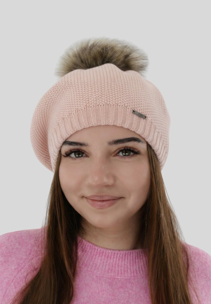 Roze gebreide baret met een grote nep bont pompon bovenop, een geribbelde band en een klein metalen accentlabel aan de zijkant.