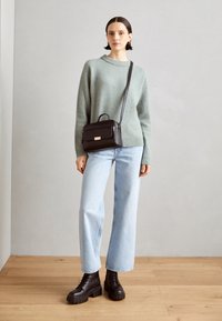 Pull en laine vert clair, jean évasé bleu clair, bottines noires épaisses à lacets, et sac bandoulière noir avec poignée supérieure et détails dorés.