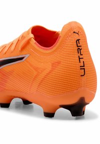 Scarpe da calcio arancioni vivaci con tomaia testurizzata, dettagli neri e tacchetti in gomma stampata per una migliore aderenza sulla suola. Presenta un design aderente.
