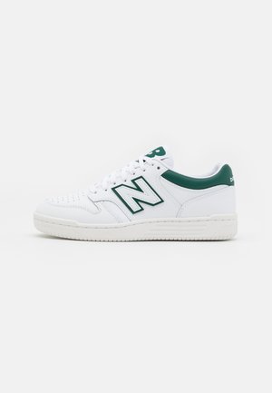 Baskets basses blanches avec des accents verts, grand logo "N" sur le côté, bout perforé et semelle blanche, présentées en profil sur un fond uni.
