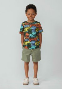 Kleurvol T-shirt met korte mouwen met een collage van landschappen in oranje, groen, blauw en geel. Gepaard met lichtgroene shorts en witte schoenen.