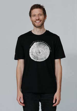 Zwart katoenen T-shirt met een circulaire boomringafbeelding in het wit, met tekst om de afbeelding heen. Korte mouwen en een ronde hals.