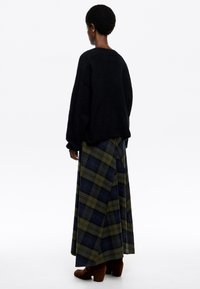 Czarny oversize sweter połączony z długą spódnicą w kratę w zielonych i niebieskich odcieniach. Całość dopełniają brązowe zamszowe botki za kostkę.