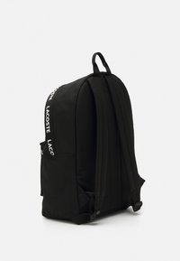 Black fabric backpack with adjustable straps, side pockets, and white logo detail. Smooth texture and streamlined design.