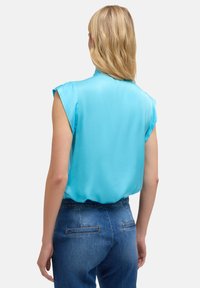Blusa a maniche corte di colore azzurro chiaro, realizzata in tessuto morbido, caratterizzata da una vestibilità rilassata e un collo rotondo, abbinata a jeans di denim scuro.