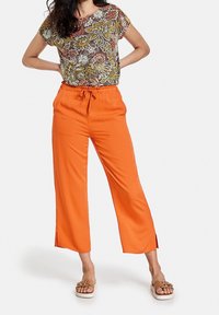 Haut floral multicolore à manches courtes et pantalon orange à jambes larges avec taille à cordon et fentes sur les côtés. Porté avec des sandales beiges.