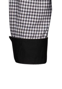 Camicia con polsini neri caratterizzata da un motivo a scacchi bianco e nero. Tessuto di cotone con una consistenza croccante, che evidenzia il contrasto tra i colori.