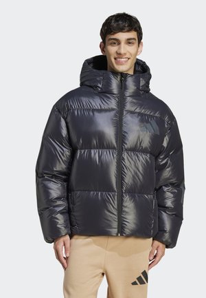 Black puffer jacket with a hood, featuring a glossy finish, quilted design, and Adidas logo on the chest. Worn over light-colored pants.