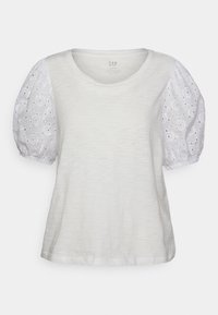 Bílý tričko s krátkými nabíranými rukávy vyrobené z vyšívané látky. Má měkkou texturu a kulatý výstřih. Jednoduchý design s volným střihem.