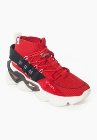 Zapatilla alta roja con parte superior de punto, correa elástica negra, suela blanca y marca "Spyder" en el lateral, en un ángulo que muestra el perfil exterior.