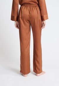 Bruine gestreepte pyjamabroek met een zachte textuur, elastische tailleband en contrasterende rode strepen, met een recht model.