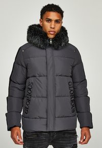 Daunenjacke in Dunkelgrau mit Kapuze aus Kunstpelz. Verfügt über vertikale Nähte und das Wort "GLORIOUS" in Schwarz auf der linken Seite. Mit Reißverschlusstaschen.