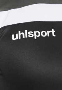 T-shirt de sport noir avec des rayures horizontales blanches et grises. Présente le logo "uhlsport" en texte blanc en gras. Texture de tissu lisse et respirante.