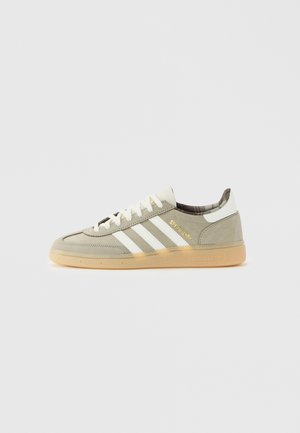 Hellgrauer Adidas Sneaker mit weißen Streifen, Gummisohle, „Spezial“-Schriftzug in Gold und tartan-gefüttertem Innenfutter, Seitenansicht.