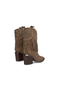 Bottines en daim marron avec des franges et des clous argentés, dotées d'un talon carré et d'un bout arrondi.