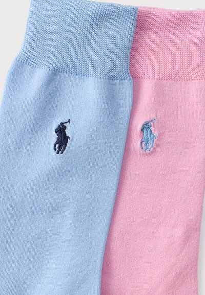 Απαλά πλεκτές κάλτσες σε απαλό γαλάζιο και ροζ χρώμα με κεντημένα λογότυπα παίκτη πόλο κοντά στις πάνω μανσέτες, τοποθετημένες δίπλα δίπλα.