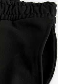 Schwarze Leggings aus geripptem Stoff mit einem gerafften Bund und seitlichen Öffnungen, die eine glatte Textur und eine figurbetonte Passform zeigen.