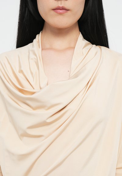 Beige draped top van gladde, lichte stof, met zachte plooien en een kraaghalslijn, benadrukt een minimalistisch ontwerp.