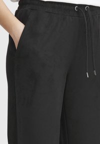 Zwarte joggingsbroek gemaakt van zachte, textuurstof. Bevat zijzakken, een elastische tailleband met trekkoorden en een subtiele glans.