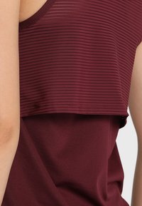 Canotta sportiva bordeaux con un design a strati caratterizzato da strisce orizzontali, texture morbida e vestibilità ampia per il massimo comfort.