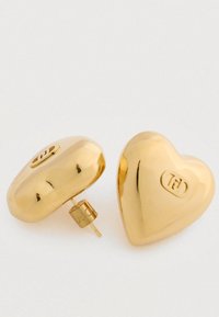 Zlaté náušnice ve tvaru srdce s hladkým, odrazivým povrchem a malým vyrytým logem na každé.