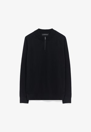 Pull noir en tricot doux. Il présente un col rond, une courte fermeture éclair sur le devant et des poignets et un ourlet côtelés.