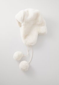 Chapeau blanc en fausse fourrure avec des rabats d'oreilles, présentant une texture douce et deux pompons sur les liens. Forme arrondie avec un design confortable.