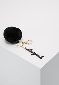 Mustapekka tekoturkis pom pom-avainpidike, jossa on kultainen metalliklipsi. Mukana musta muovinen riipus, jossa lukee "Ikuisesti" kauniilla kirjaimistolla.