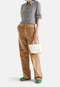 Svart-vit rutigt knäppt skjorta, tan corduroy vida byxor, vit handväska med präglad design och gröna skor.