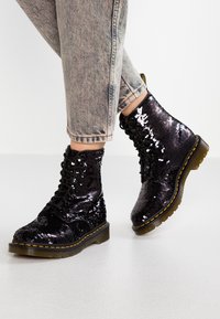 Botines de tacón bajos negros con lentejuelas, puntera redonda, cordones en la parte delantera y detalle de costura amarilla. Suela de goma gruesa con un acabado texturizado.