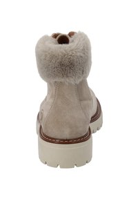 Botín de ante beige con un suave cuello de piel, punta redonda y suela de goma ligera en contraste. Presenta costuras decorativas y un pequeño logotipo.
