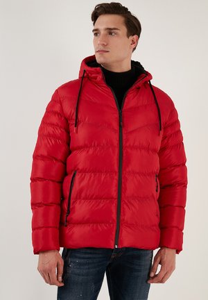 Rote Daunenjacke mit Kapuze, versehen mit gestepptem Textil, einem Reißverschluss vorne und schwarzen Akzenten. Getragen über einem schwarzen Rollkragenpullover für einen Kontrast.